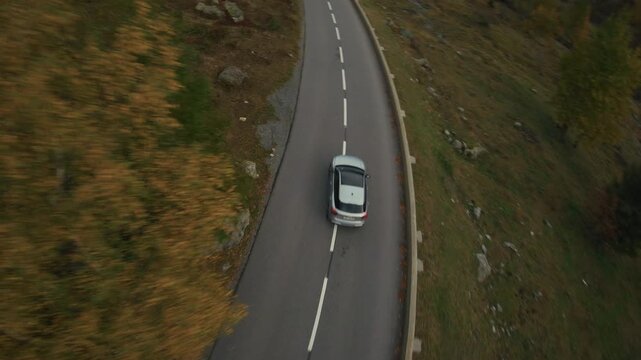 High-speed FPV drone footage of a sporty car driving aggressively over the Col des Montets mountain pass near Chamonix during autumn with colorful foliage fast cornering and dynamic alpine road action