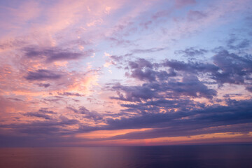 Fototapeta premium Soft lavender and peach clouds drift across a tranquil Mediterranean Sea at sunset, with gentle light reflecting on the water and creating a peaceful, atmospheric mood.