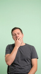 Tired Man Yawning And Covering His Mouth On Green Background