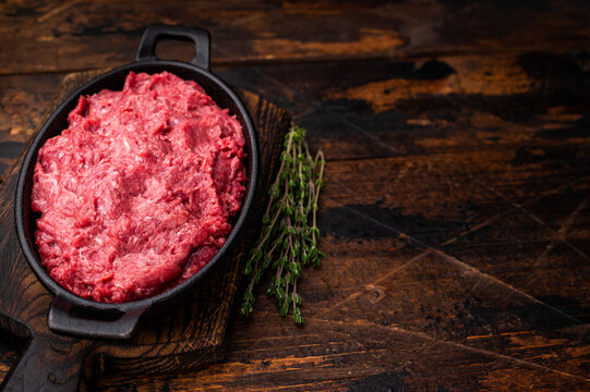 Uncooked venison mince with pink pepper and fresh herbs on a wooden cutting board. Overhead view for a premium food concept.