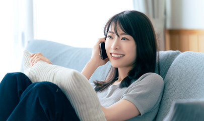 自宅のソファでスマートフォン通話を楽しむ女性,リラックスした日常のひととき, A Woman Enjoying a Phone Call While Relaxing on a Sofa at Home © Trickster*
