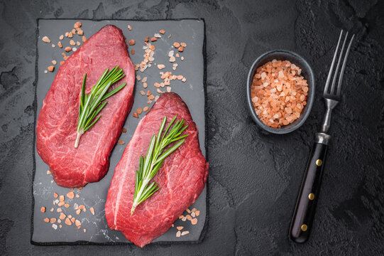 Marbled Wagyu beef chuck top blade steak similar to angus and yakiniku cuts displayed with rosemary on dark textured backdrop great for steakhouse food stock.