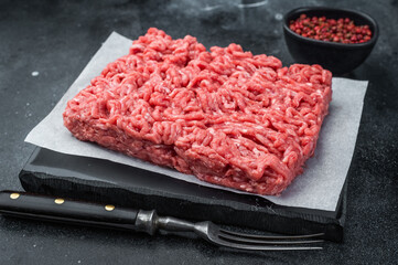 Raw forcemeat with spices and fork on dark stone surface providing high detail for culinary, kitchen and ingredient stock use. © Mironov