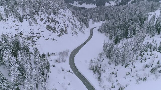 Forward moving drone shot flying along a snowy mountain road during winter whiteout near Col du Pillon Les Diablerets Gstaad showing alpine landscape cold weather and dramatic Swiss Alps scenery