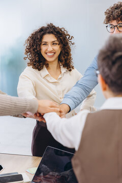 Diverse business team stacking hands in a shared moment of collaboration, unity, and success in a modern office