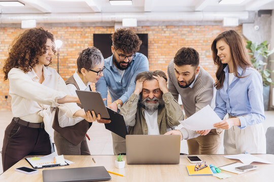 Overwhelmed senior employee experiencing burnout at work with young colleagues demanding attention and tasks, office pressure