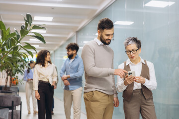 Obraz premium Diverse colleagues looking at smartphone, collaborating and discussing business strategy in an office hallway