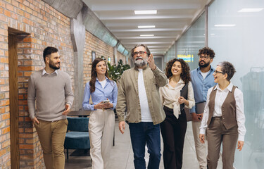 Obraz premium Diverse business team walking and talking in a modern office hallway, collaborating, smiling, and discussing work