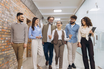 Diverse business team smiling and communicating while walking together in a modern office hallway