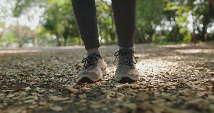 Ground level view shows a woman mid jump as she skip ropes on a paved path in an urban park. Grey knit sneakers and dark leggings stay sharp as the rope arcs.