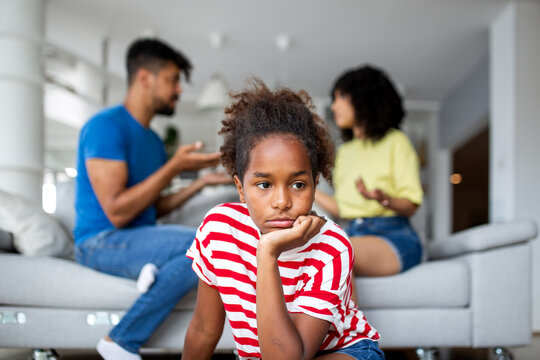Pensive African American kid resting head on hand while parents fight in the background. Concept of domestic conflict, childhood anxiety, family problems, and the emotional toll of parenting.