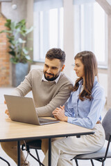 Professional man and woman collaborating, discussing information on a laptop during an office...
