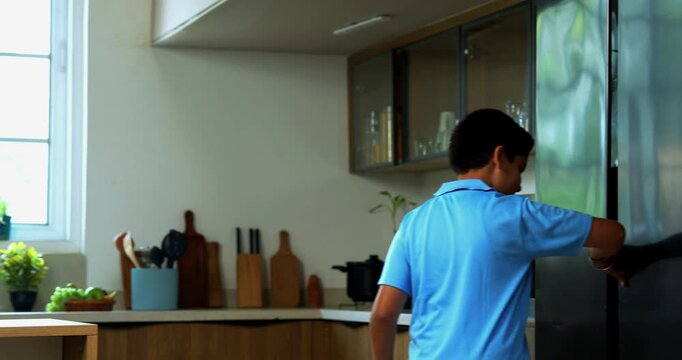 Indian asian young kid eating laddoo from fridge while father catches him sneaking sweets silently at night, both laughing together in modern kitchen creating funny family bonding moment