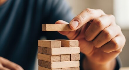 Close-up of a hand stacking slender wooden blocks into a vertical tower, capturing focus, tension, and the delicate balance of strategic building play

