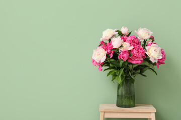Fototapeta premium Vase with beautiful peony flowers on stool near green wall in room, closeup