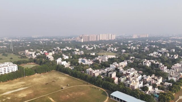 Drone footage of Greater Noida&mdash;quiet residential blocks and tree-lined streets in the foreground, transitioning to expansive green zones and high-rise housing developments in the distance.