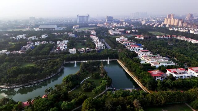 Aerial footage of Greater Noida's landscaped urban lake with curved walkways, fountains, and dense greenery, forming a calm green oasis amid the surrounding cityscape.