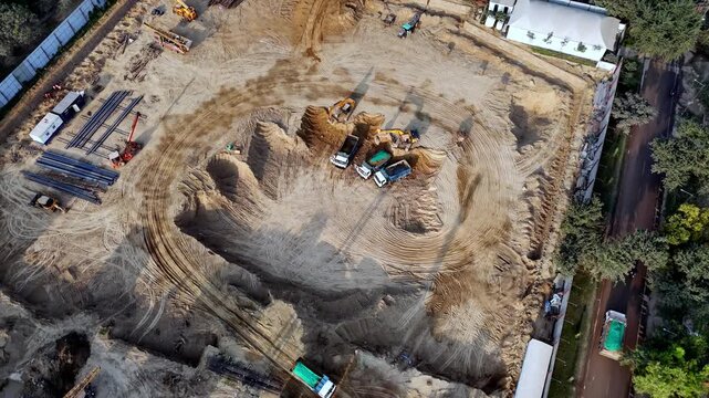 Drone footage capturing an under-construction plot where excavators and trucks reshape the land, revealing patterns of earthworks, foundations in progress, and the scale of modern urban construction.
