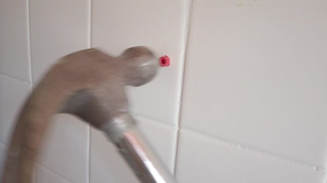 Close up of hammer inserting plastic wall plug into tiled wall during installation.