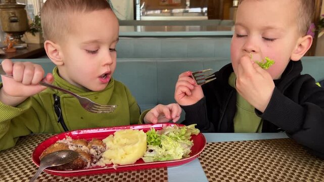 Two Boys Tasting Salad At Table, Playful Sibling Mealtime With Lettuce, Mashed Potatoes, Fork And Spoon, One