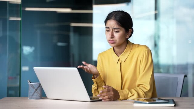 Frustrated young businesswoman sitting at desk in modern office having difficulty working on laptop. Confused female employee faces technical problem or error while trying to complete her task.