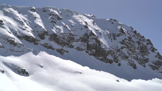 Panoramic snowy mountain range shows jagged rocky peaks, ridgeline contours, clear sky. Wide cinema vista reveals ice covered highland summits, crags, crest forms, azure backdrop.
