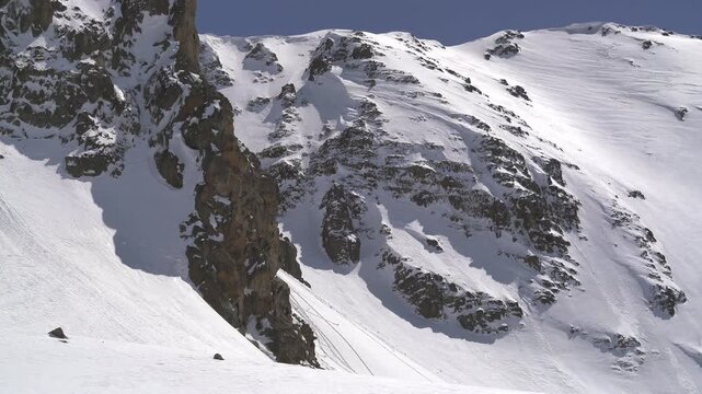 Panoramic snowy mountain range shows jagged rocky peaks, ridgeline contours, clear sky. Wide cinema vista reveals ice covered highland summits, crags, crest forms, azure backdrop.