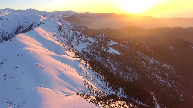 Aerial sunrise over snowy Alps peaks above a forested valley, warm morning glow. Overhead dawn sun touches icecapped ridgelines, showing pine basins across Europe.