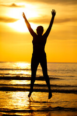 A woman is jumping in the water at sunset