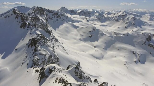 Aerial winter panorama shows snowy Alps mountain ridges and glaciers across vast peaks. Cinematic high altitude scenery reveals pristine white summits, icy slopes, remote European wilderness.