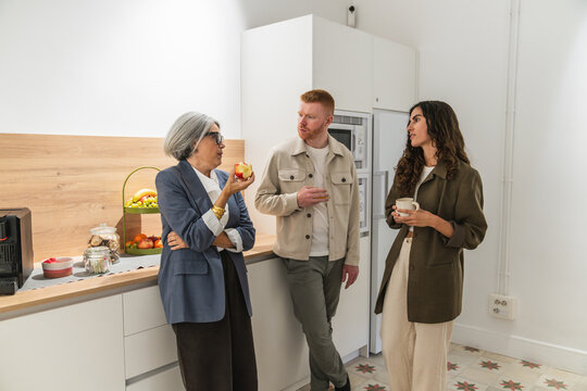 Three diverse colleagues interacting and discussing various topics in a modern coworking office kitchen during a coffee break