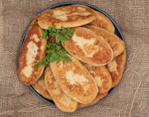 Golden fried potato pies arranged on a plate with fresh parsley. Classic homemade comfort food photographed on rustic burlap fabric, ideal for traditional cuisine and cooking themes.