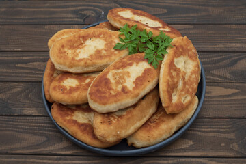 Golden fried potato pies arranged on a plate with fresh parsley. Classic homemade comfort food photographed on rustic wooden background for culinary use.