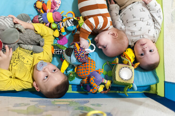 In a bright playpen, three brothers are happily exploring their vibrant toys. The playful energy of the twins and their older sibling lights up the room as they interact joyfully