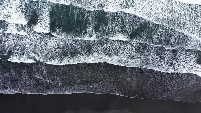 Slow motion aerial view of waves rushing to the shore on black volcanic sand. Atlantic Ocean, Iceland by drone
