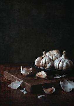 Bulbs and cloves of fresh garlic scattered on dark wooden board.