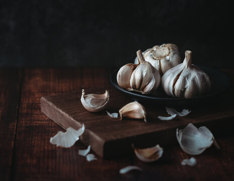 Bulbs and cloves of fresh garlic scattered on dark wooden board.