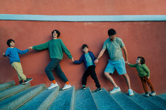 Family group holding hands walking on outdoor staircase in summer