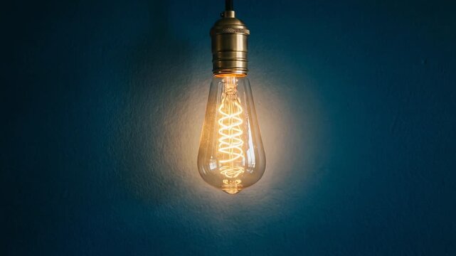 Glowing vintage Edison light bulb with warm filament on dark blue textured wall background