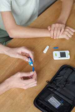 Hands performing blood glucose check with glucometer on table