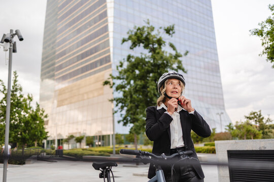 Businesswoman fastening helmet by bicycle on city street outdoors