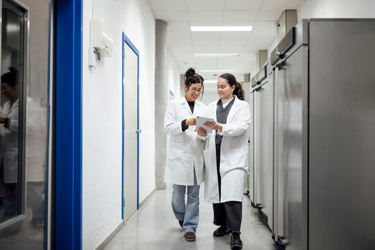 Scientists in lab coats discussing research on tablet in hallway