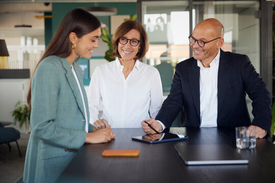Smiling businessman and woman explaining co worker at office