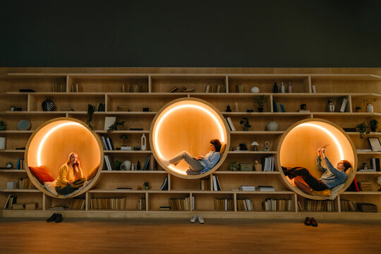 People relaxing with technology in illuminated circular seats at library