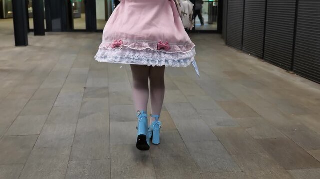 Woman walking on a tiled ground in a pink dress and blue high heel shoes