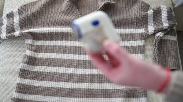 Woman cleaning fabric shaver full of lint while removing pills from sweater at home