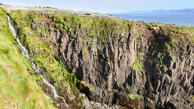 Small waterfall flowing into Dingle Bay and the Atlantic Ocean, along rocky coastline near the village of Ventry, off Slea Head Drive on the Dingle Peninsula in County Kerry, Republic of Ireland.