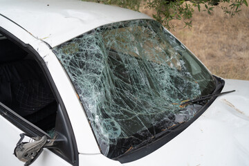 White car with a completely shattered windshield, broken glass, and damaged exterior after a serious road accident