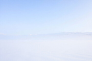 Fototapeta premium Serene landscape captured from above with fog, clouds, and a clear blue sky in a breathtaking aerial view