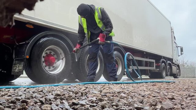 Worker in high visibility clothing cleaning white semi truck wheels with professional pressure washer